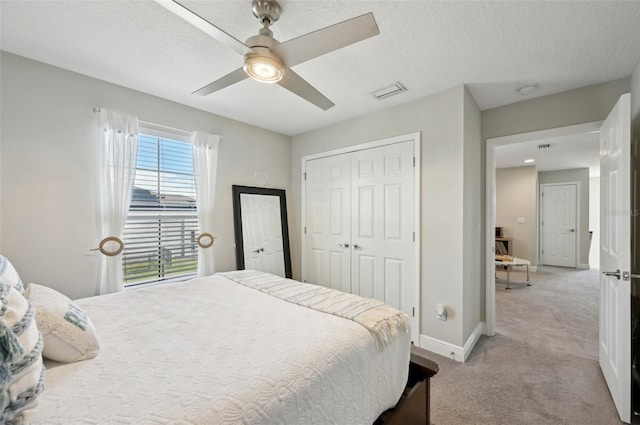 bedroom with ceiling fan, baseboards, light carpet, a closet, and a textured ceiling