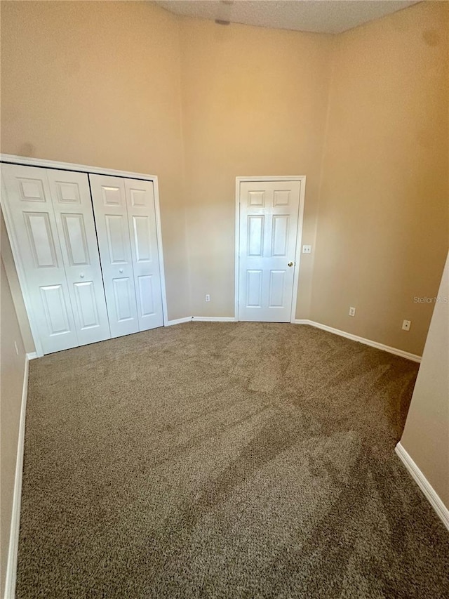 unfurnished bedroom featuring baseboards, carpet floors, a high ceiling, and a closet