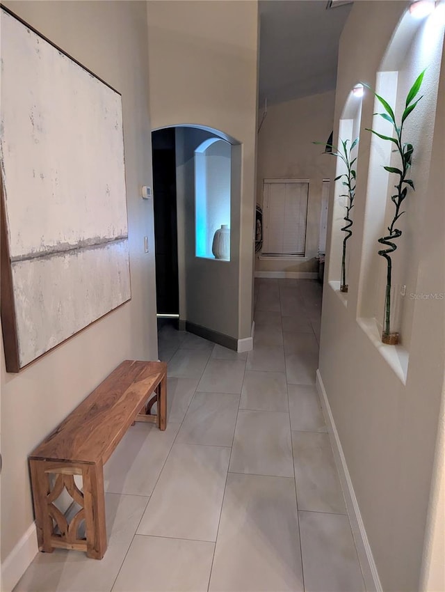 corridor with arched walkways, light tile patterned floors, and baseboards