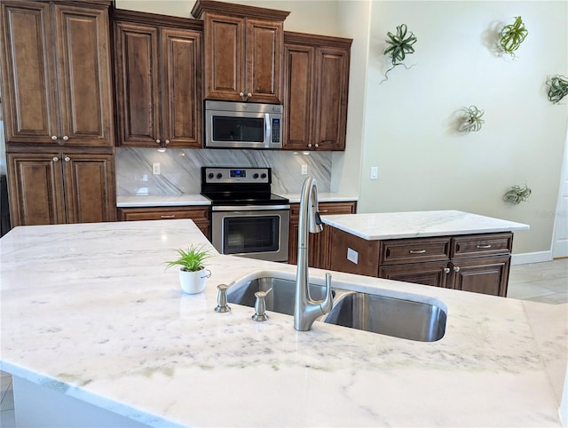 kitchen featuring a sink, light stone countertops, backsplash, and stainless steel appliances