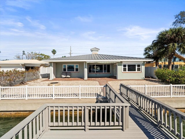 rear view of property featuring stucco siding, metal roof, a fenced front yard, and a standing seam roof