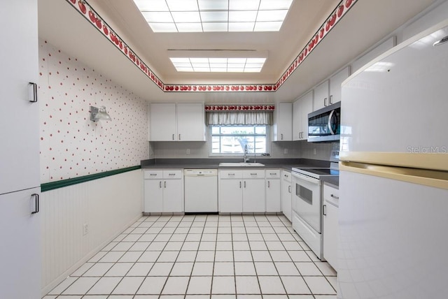 kitchen featuring white appliances, wallpapered walls, a sink, white cabinetry, and dark countertops