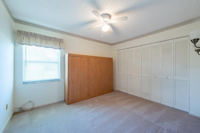 unfurnished bedroom with a ceiling fan, a closet, a textured ceiling, crown molding, and light carpet