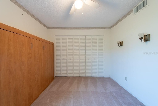 unfurnished bedroom featuring light colored carpet, visible vents, a closet, and a textured ceiling