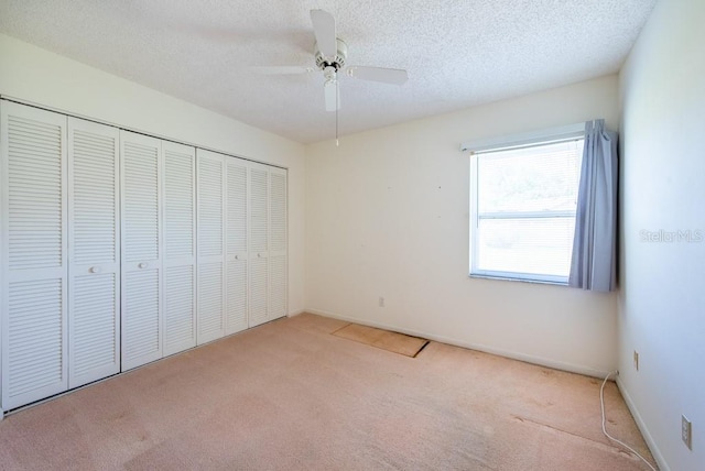 unfurnished bedroom featuring baseboards, carpet flooring, a closet, a textured ceiling, and a ceiling fan