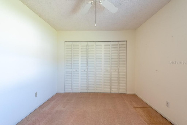 unfurnished bedroom with a textured ceiling, ceiling fan, a closet, and light carpet