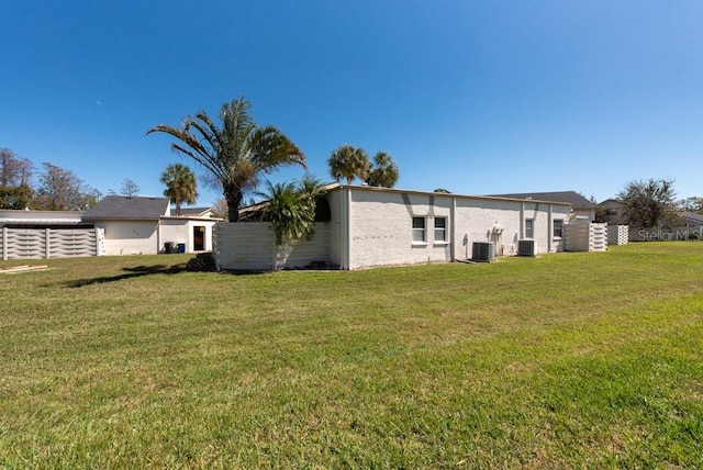 rear view of house with a yard, central AC unit, and fence