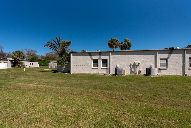 rear view of property featuring central air condition unit, a lawn, and stucco siding