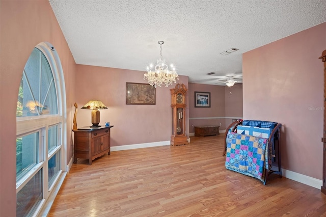 interior space with light wood-type flooring, visible vents, ceiling fan with notable chandelier, a textured ceiling, and baseboards