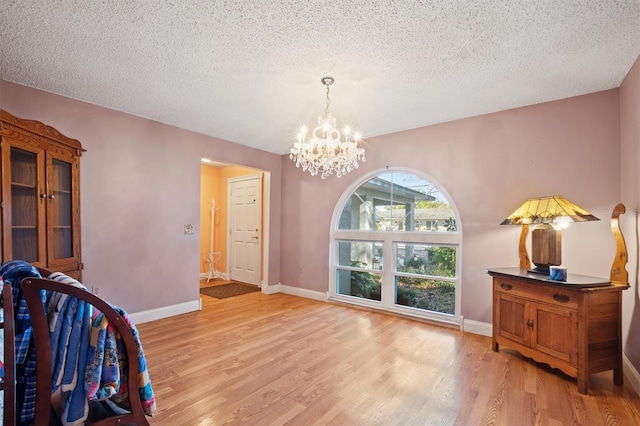 interior space featuring a chandelier, light wood finished floors, a textured ceiling, and baseboards