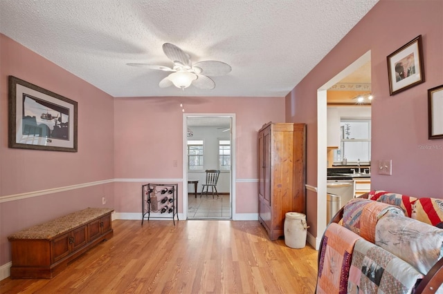 interior space featuring a textured ceiling, light wood-style floors, baseboards, and ceiling fan