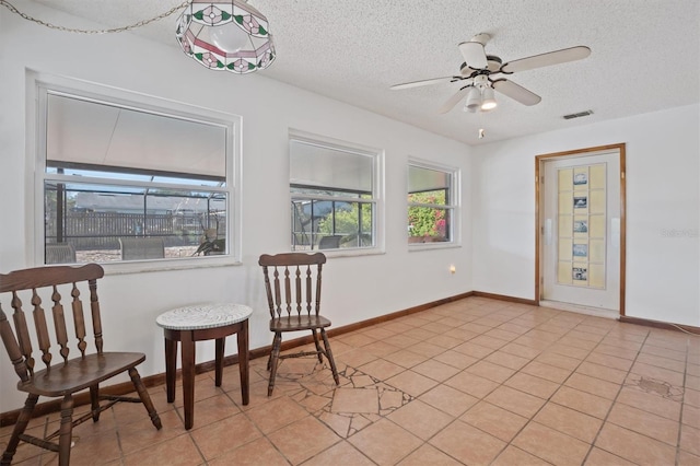 living area featuring visible vents, baseboards, ceiling fan, light tile patterned floors, and a textured ceiling