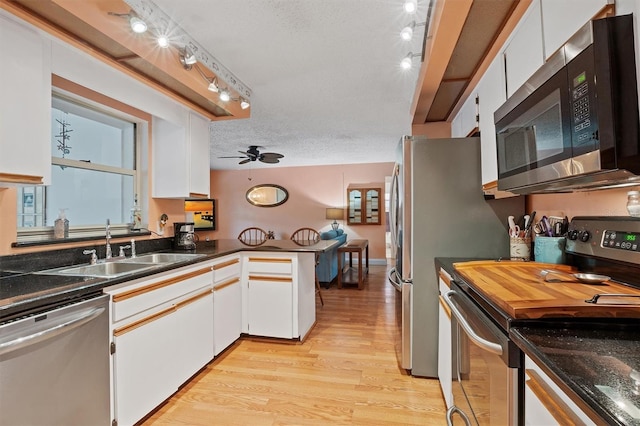 kitchen with light wood finished floors, appliances with stainless steel finishes, a textured ceiling, white cabinetry, and a sink