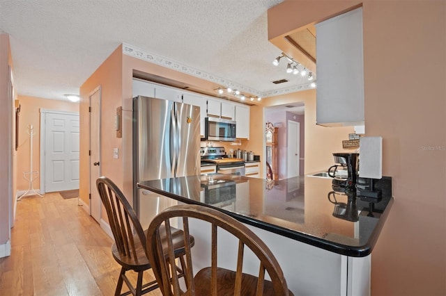 kitchen with dark countertops, a textured ceiling, stainless steel appliances, a peninsula, and white cabinets