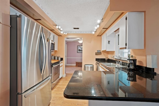 kitchen with a ceiling fan, a sink, light wood-style floors, appliances with stainless steel finishes, and a textured ceiling