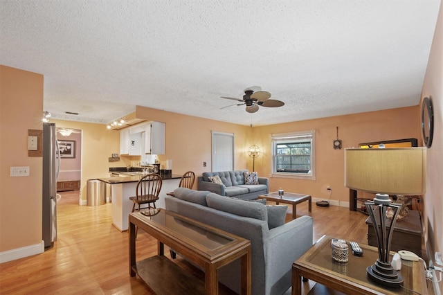 living room featuring baseboards, a textured ceiling, a ceiling fan, and light wood finished floors