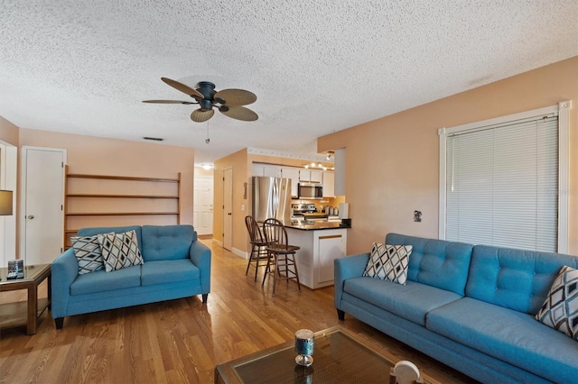 living area with baseboards, a textured ceiling, light wood-style flooring, and a ceiling fan