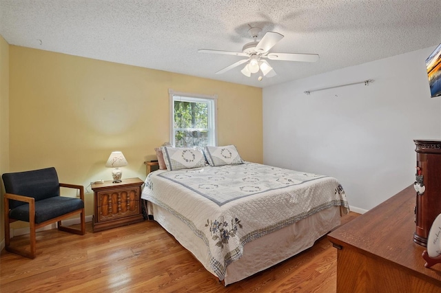 bedroom with ceiling fan, baseboards, a textured ceiling, and light wood-style flooring