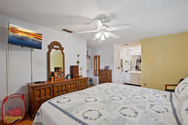 bedroom with ensuite bath, visible vents, a textured ceiling, and a ceiling fan