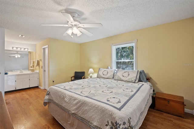 bedroom with baseboards, a textured ceiling, ensuite bathroom, and light wood finished floors