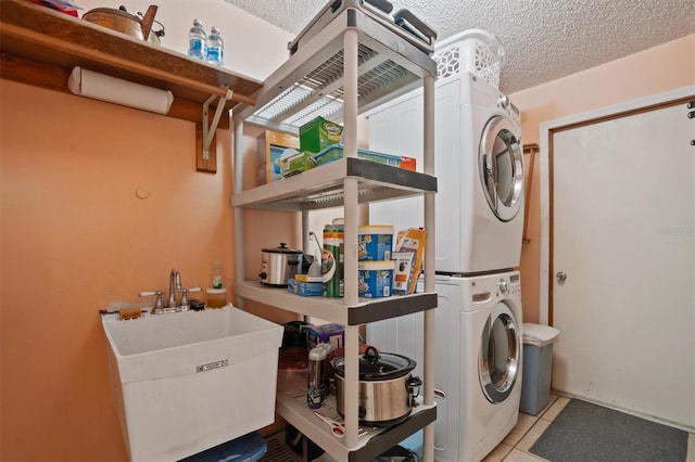 laundry room with laundry area, stacked washer and clothes dryer, light tile patterned flooring, a textured ceiling, and a sink