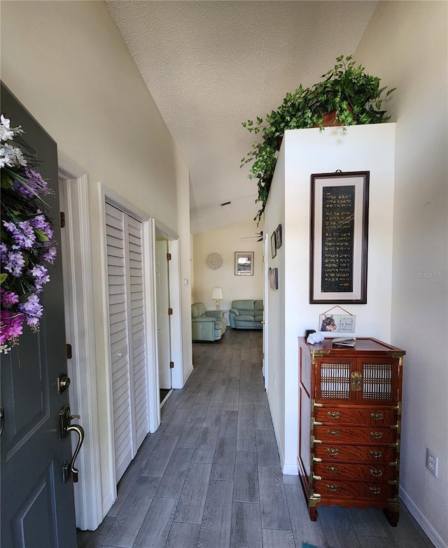 hallway with dark wood finished floors, lofted ceiling, baseboards, and a textured ceiling