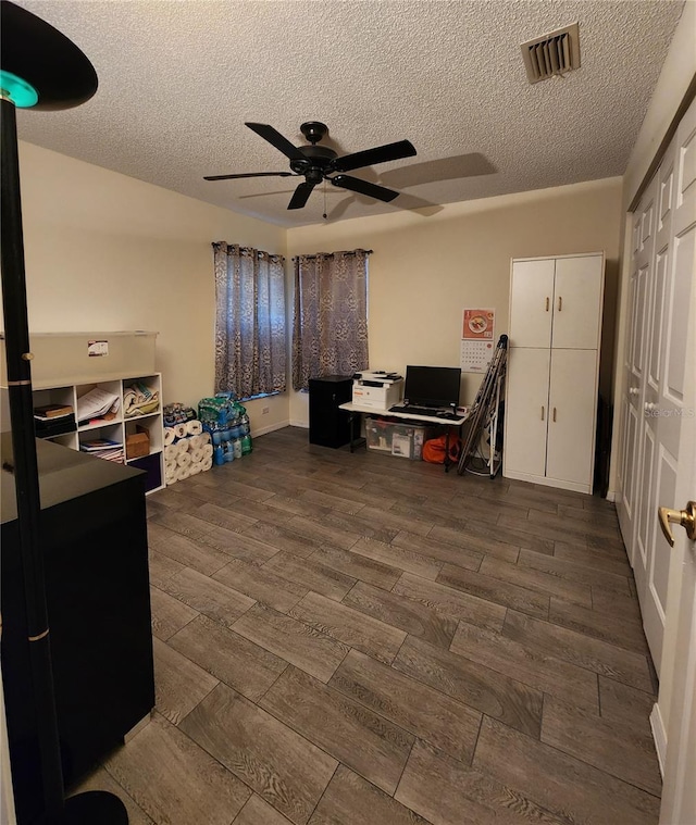 home office with dark wood finished floors, visible vents, a textured ceiling, and a ceiling fan