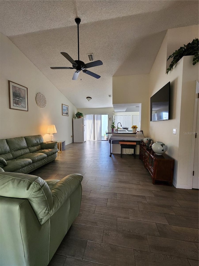 living area featuring a ceiling fan, visible vents, wood tiled floor, lofted ceiling, and a textured ceiling