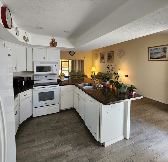 kitchen featuring a sink, white appliances, dark countertops, and wood finish floors