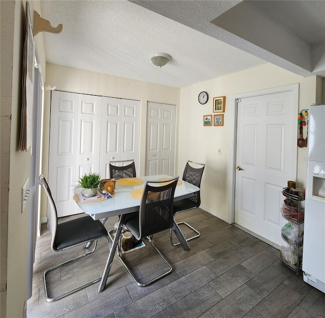 dining space with a textured ceiling, baseboards, and wood finish floors