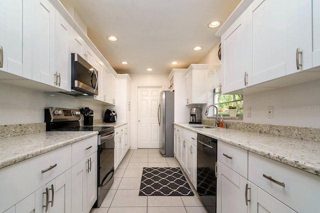 kitchen featuring light tile patterned floors, a sink, white cabinets, appliances with stainless steel finishes, and backsplash