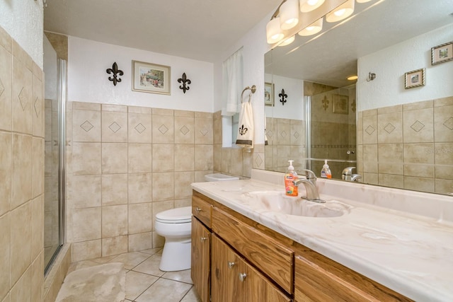 full bathroom featuring toilet, vanity, a tile shower, tile patterned floors, and tile walls