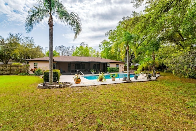 back of property featuring fence, stucco siding, a lawn, a sunroom, and an outdoor pool