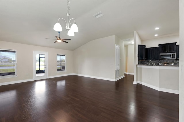 unfurnished living room with visible vents, ceiling fan with notable chandelier, dark wood finished floors, baseboards, and lofted ceiling