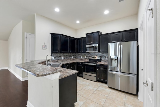 kitchen with a sink, backsplash, appliances with stainless steel finishes, a peninsula, and dark cabinets