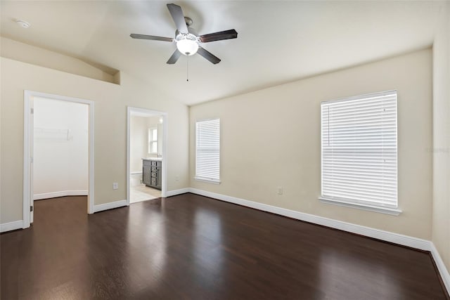 unfurnished bedroom featuring a spacious closet, dark wood-style flooring, baseboards, and vaulted ceiling