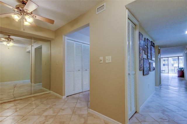 hall featuring light tile patterned floors, baseboards, and visible vents