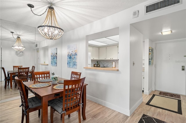 dining space with visible vents, a textured ceiling, light wood-style floors, an inviting chandelier, and baseboards