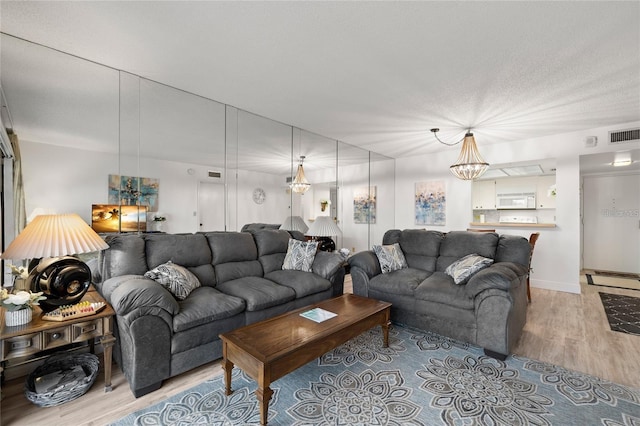 living room featuring a chandelier, visible vents, light wood-style flooring, and a textured ceiling