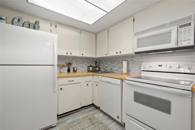 kitchen featuring a sink, white appliances, light wood finished floors, decorative backsplash, and light countertops