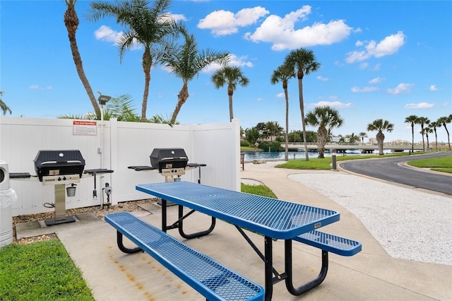 view of patio with a grill, a water view, and fence