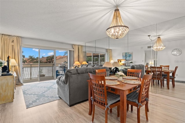 dining space featuring light wood-style floors, a textured ceiling, visible vents, and a chandelier