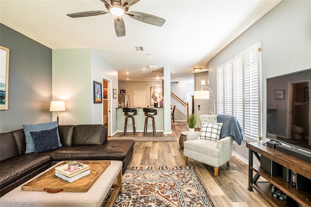 living area with stairway, wood finished floors, baseboards, and ceiling fan