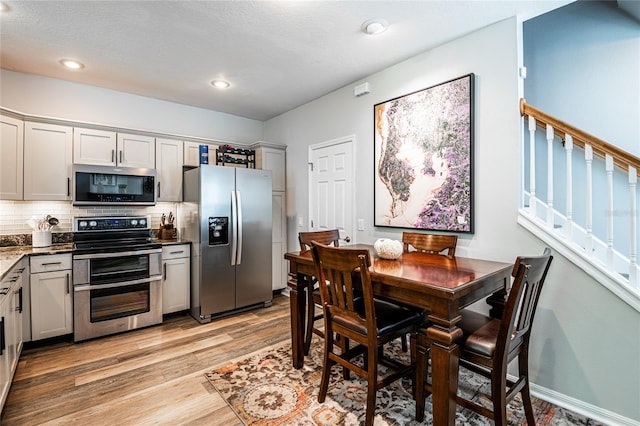 kitchen featuring backsplash, recessed lighting, light wood-style flooring, dark stone countertops, and stainless steel appliances