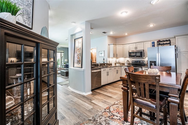 kitchen with light wood finished floors, a sink, stainless steel appliances, white cabinets, and backsplash