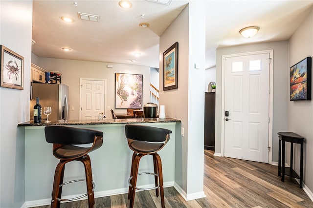 kitchen featuring visible vents, dark wood-style flooring, a breakfast bar area, and stainless steel fridge with ice dispenser