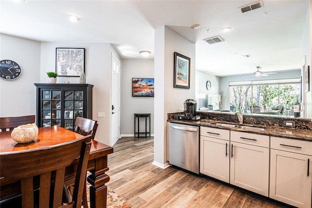 kitchen with a sink, visible vents, stainless steel dishwasher, and dark stone countertops