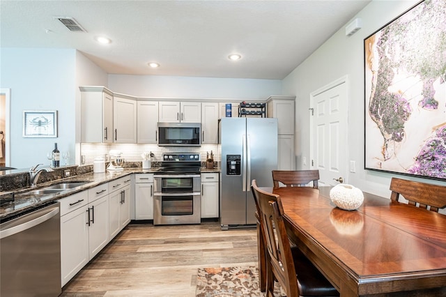 kitchen with visible vents, dark stone counters, a sink, stainless steel appliances, and light wood-type flooring