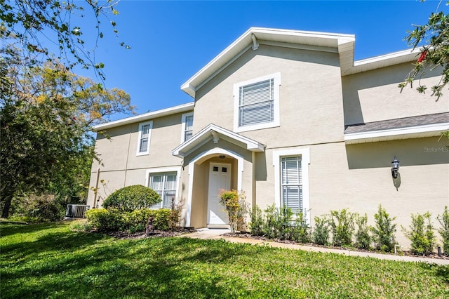 traditional-style home with a front yard, cooling unit, and stucco siding