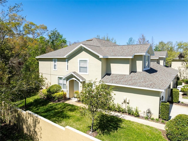 view of front of home with stucco siding, a shingled roof, a front lawn, and fence